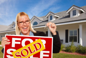 Beautiful Female Holding Keys to a New House & Sold Real Estate Sign.